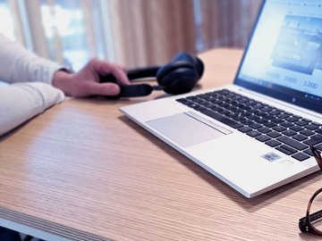 Smiling woman with long brown hair in an office sits in front of her laptop.